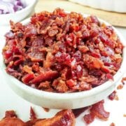a bowl of bacon bits with cooked bacon bits on the side