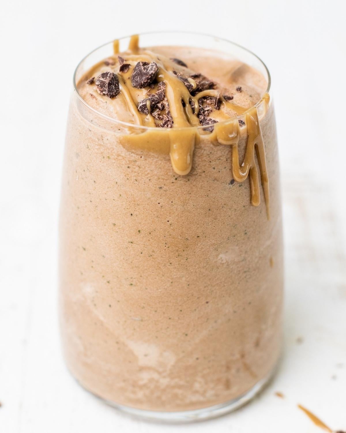a glass jar filled with chocolate peanut butter smoothie and topped with peanut butter and chocolate chips