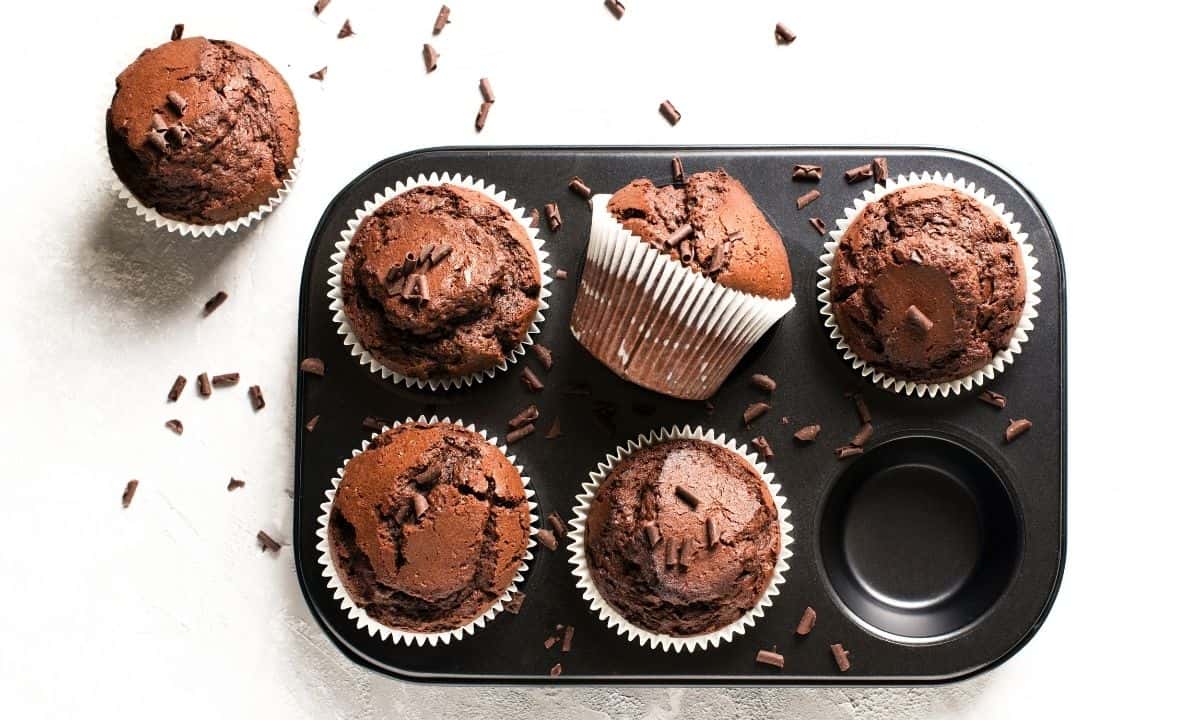 muffin pan with five chocolate zucchini muffins and one on the side
