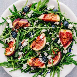 top view of an arugula fig salad arranged on a white dish