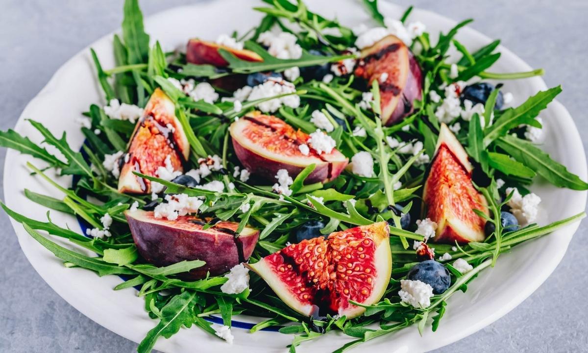 arugula fig salad arranged on a white dish
