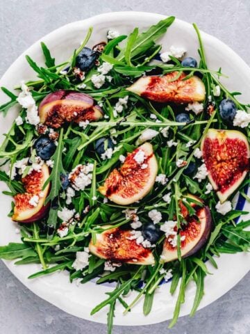 top view of arugula fig salad arranged on a white dish
