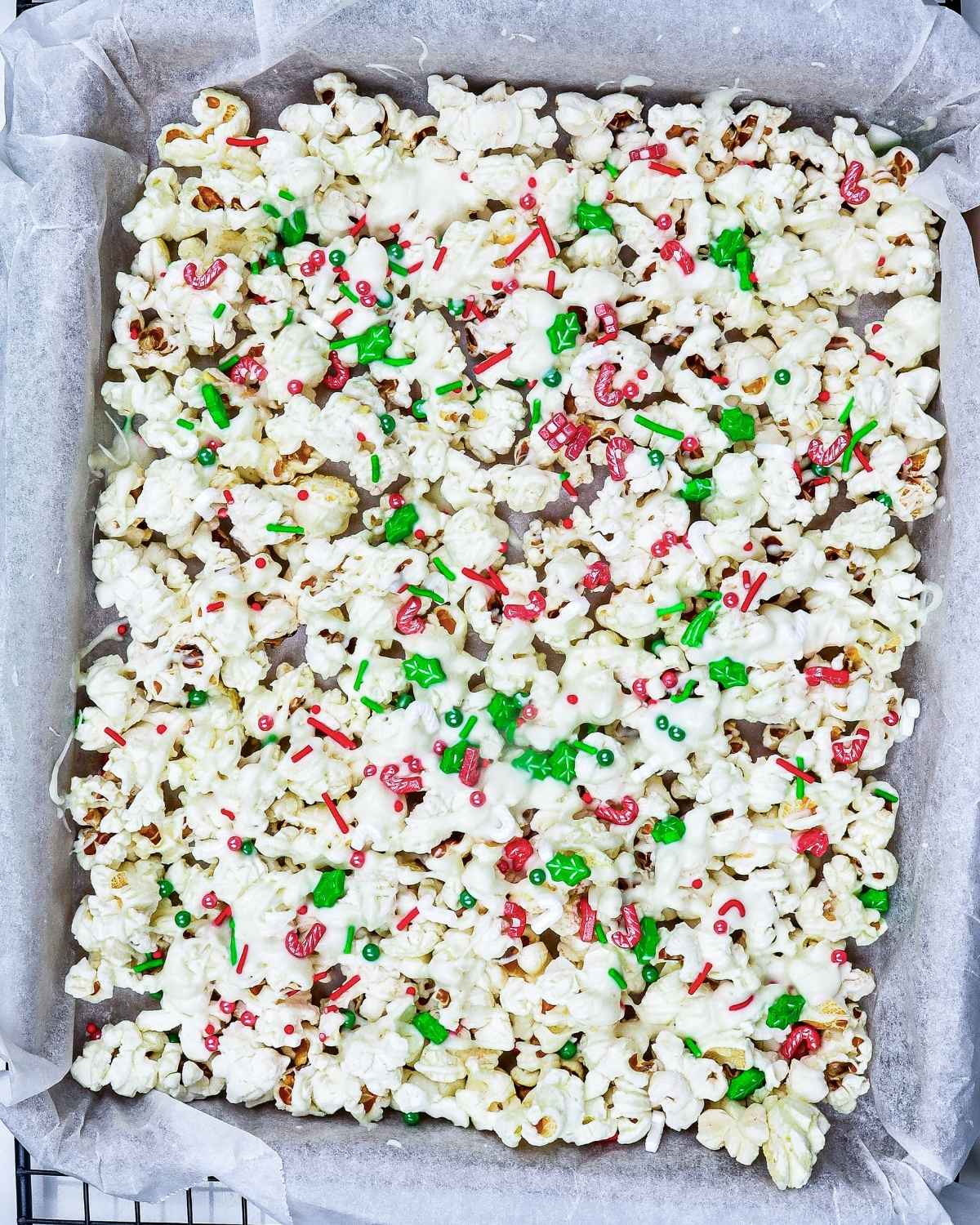 large amount of white chocolate popcorn with red and green candies spread out on a baking sheet