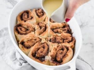 baked cinnamon rolls being drizzle with a glaze