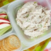 a lunchbox with crackers, sliced apples and celery, and chicken salad in the biggest compartment