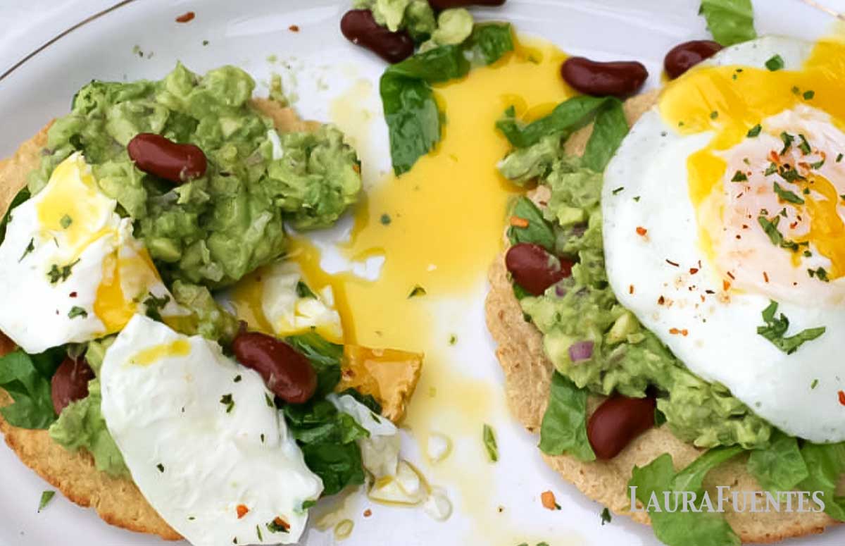 overhead view of guacamole tostadas with fried eggs on a white plate