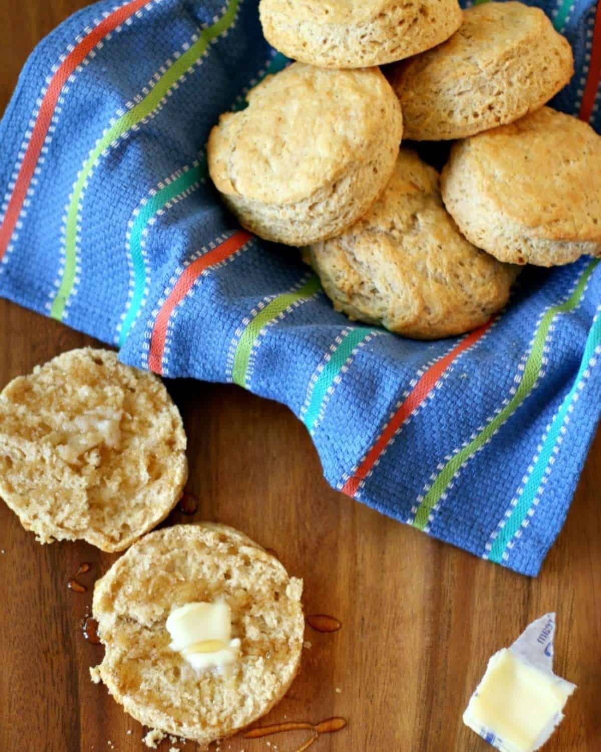 a basket of honey wheat biscuits and one sliced in half with butter on top