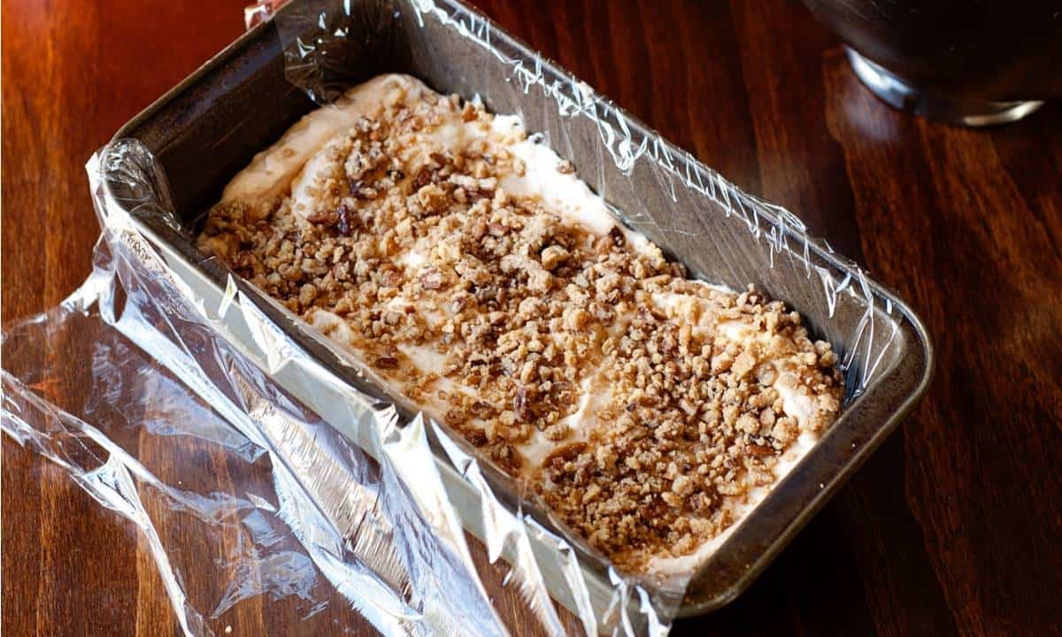 loaf pan lined with plastic wrap and frozen pumpkin pie on it