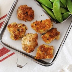 lunchbox with six chicken nuggets and veggies on the side.