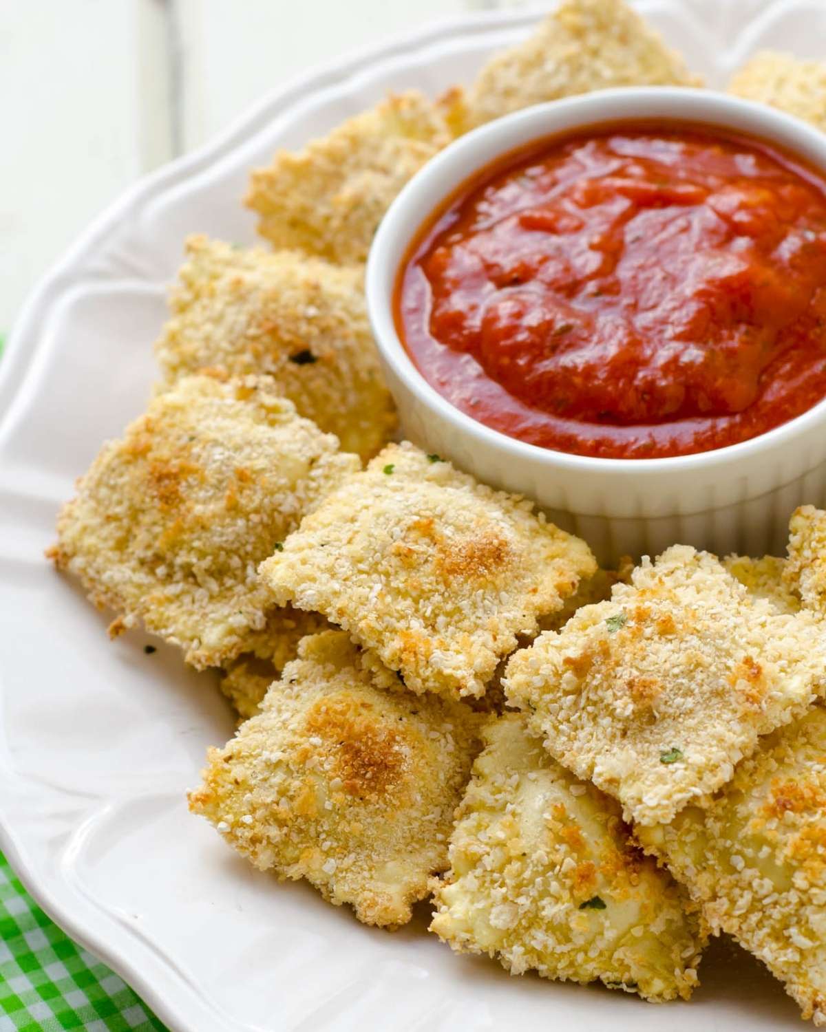 a white dish with baked ravioli surronding a small bowl of marinara sauce