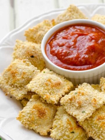 a white dish with baked ravioli surronding a small bowl of marinara sauce