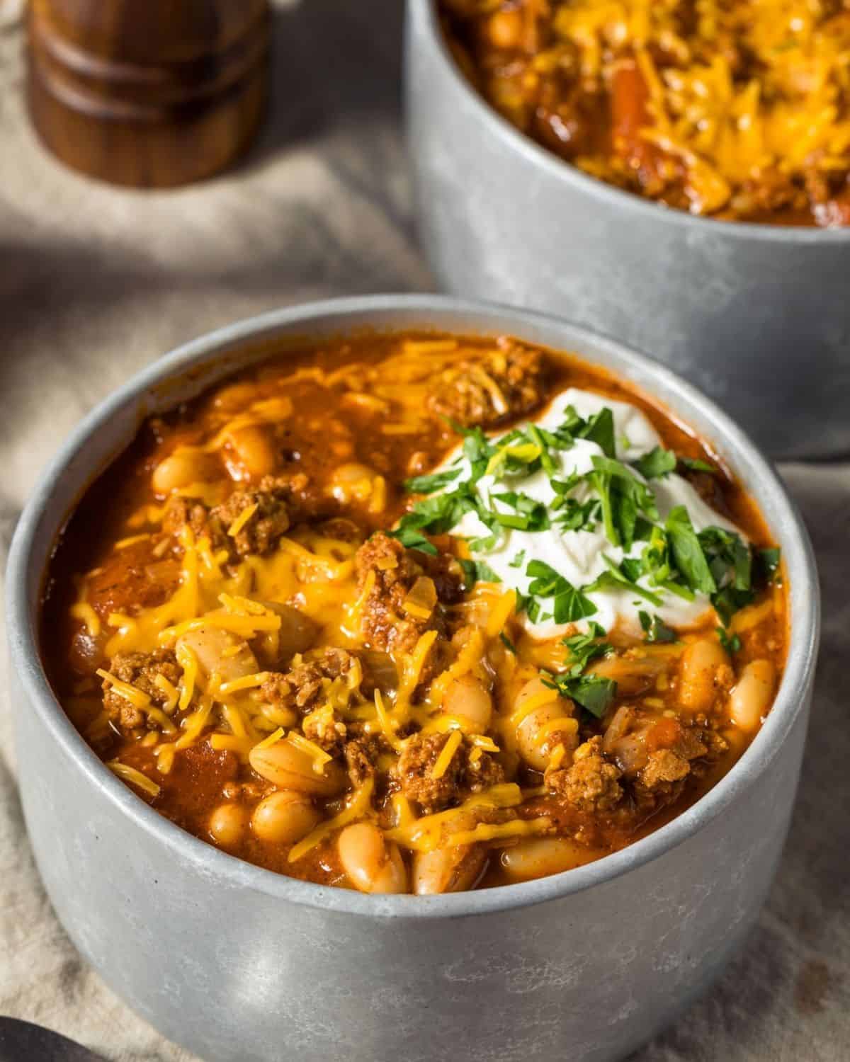 overhead view of a bowl filled with turkey pumpkin chili topped with a little sour cream and chives, another bowl in background