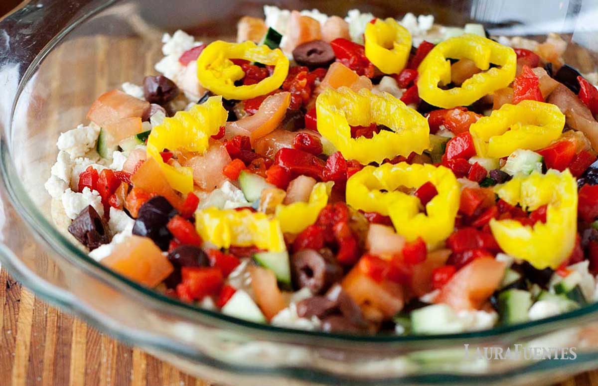 layered hummus dip in a glass bowl on a wooden board