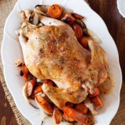 roasted chicken on a bed of roasted vegetables on a white plate on a kitchen table