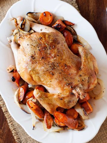 roasted chicken on a bed of roasted vegetables on a white plate