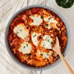 overhead view of a skillet with lasagna made with lasagna noodles, tomato sauce, meat, and cheeses using a wooden serving spoon to serve