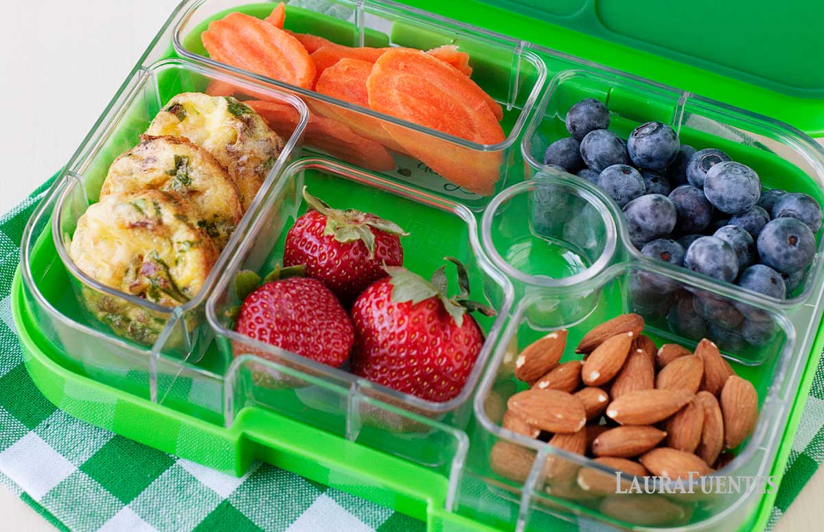 spinach and bacon mini quiches in a green lunchbox with carrot slices, blueberries, almonds and strawberries
