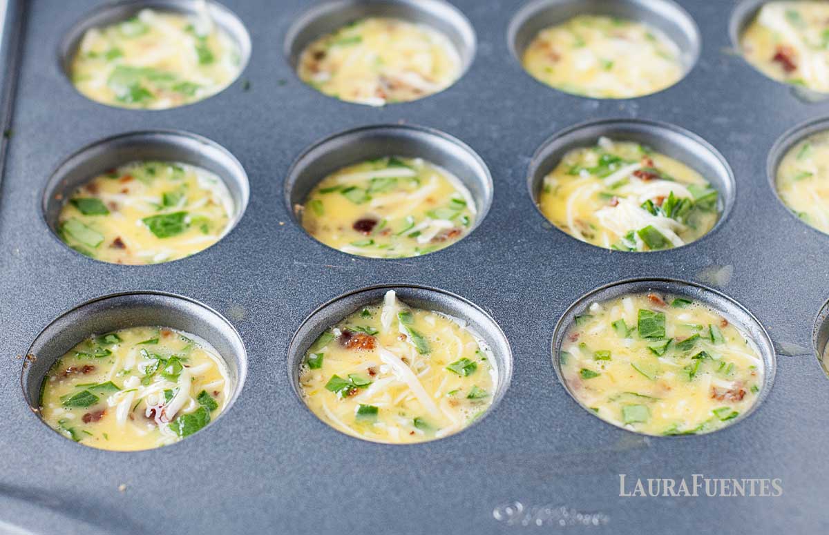 bacon and spinach mini quiches in a tin baking tray ready to be baked