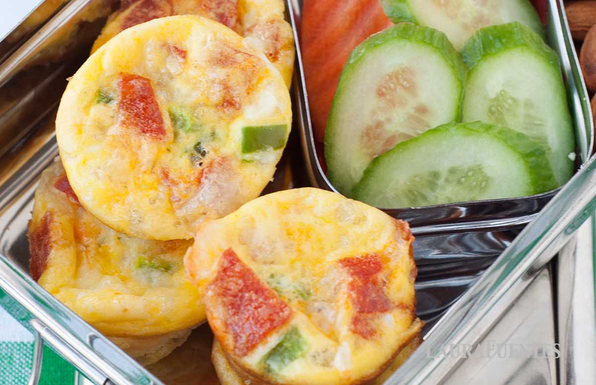 pizza mini quiches in a metal lunch box with cucumber slices, carrot slices and almonds