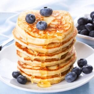 stack of fluffy gluten free vegan pancakes on a plate topped with blueberries and a little syrup