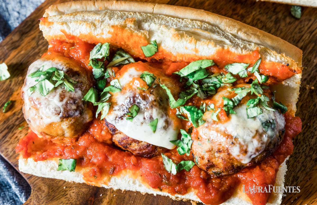 three large meatballs on a sub with red sauce and cheese