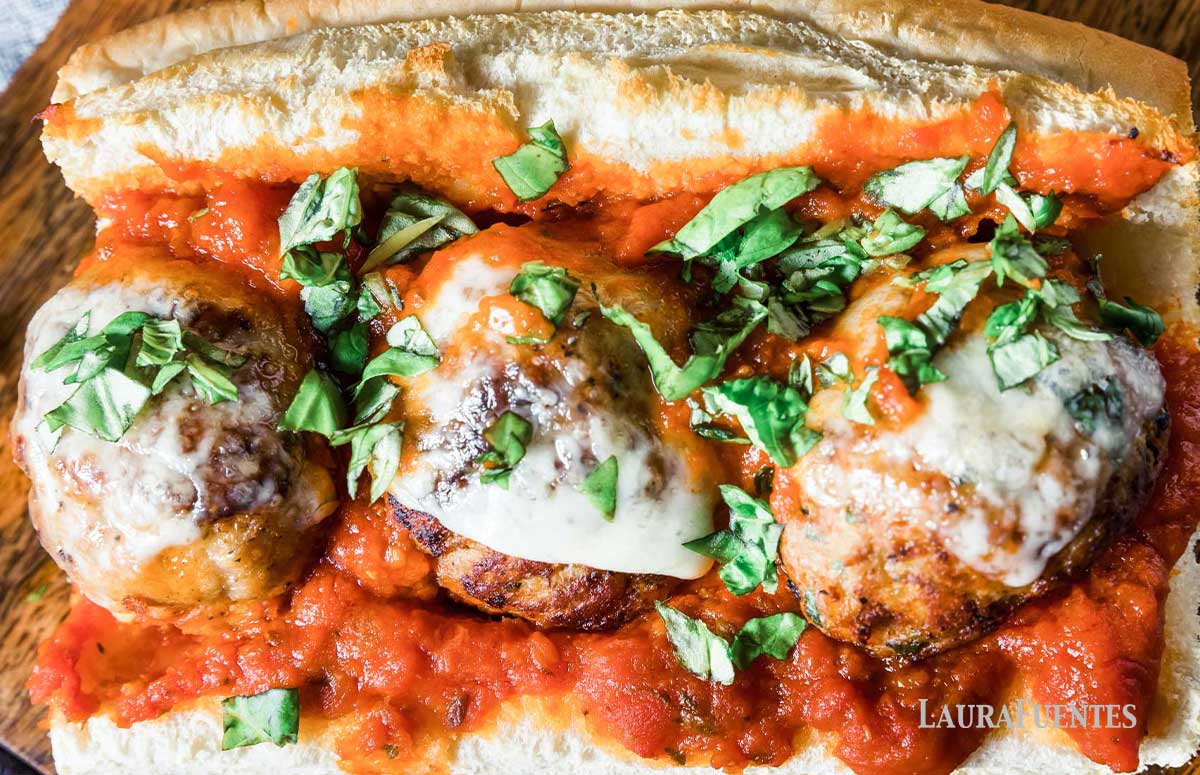 three large meatballs on a sub with red sauce and cheese