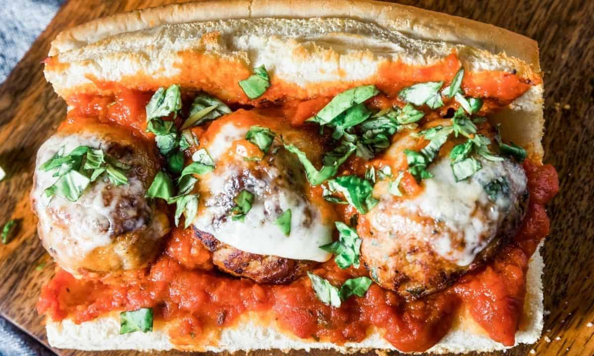 three large meatballs on a sub with red sauce and cheese