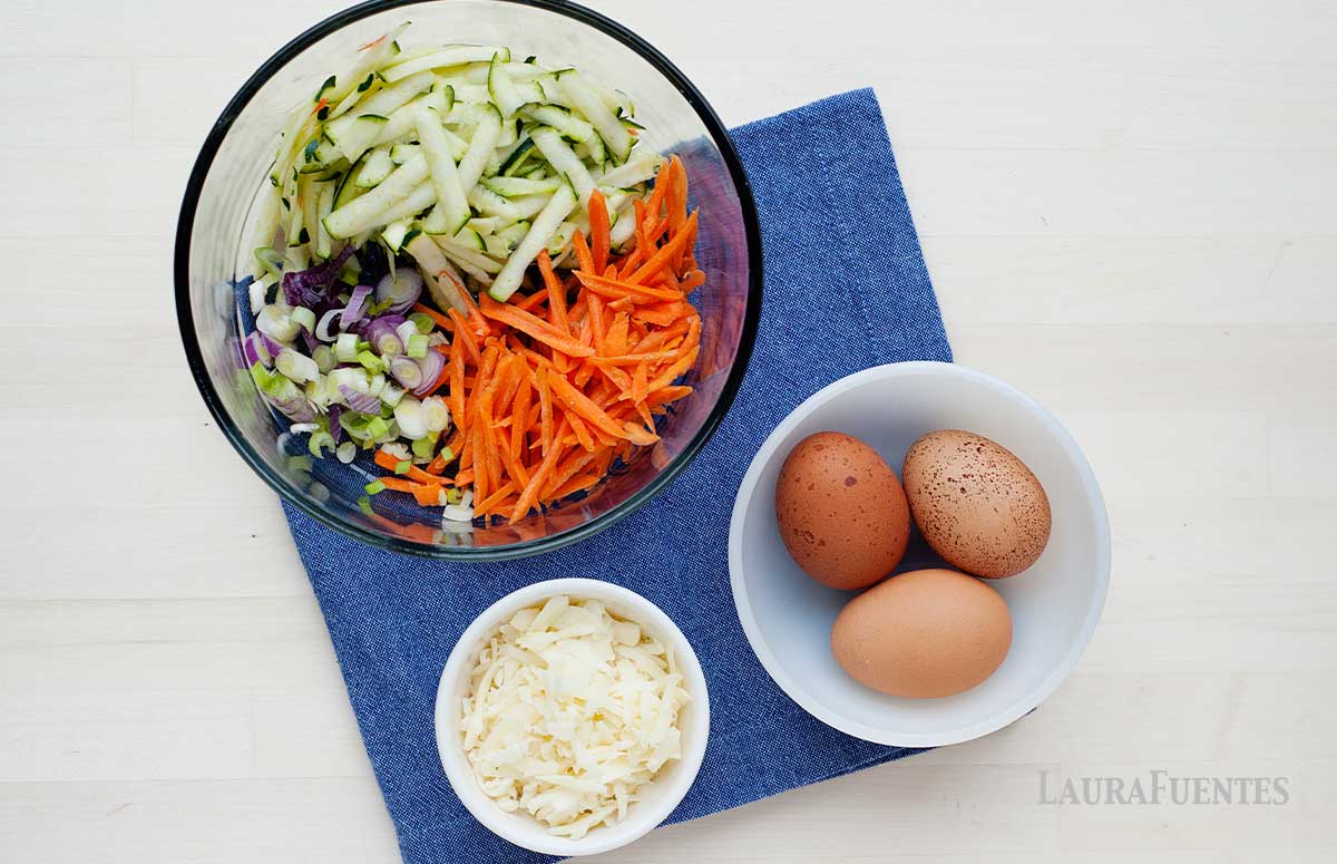 bowl of grated vegetables, next to bowl with three brown eggs and small dish of white shredded cheese