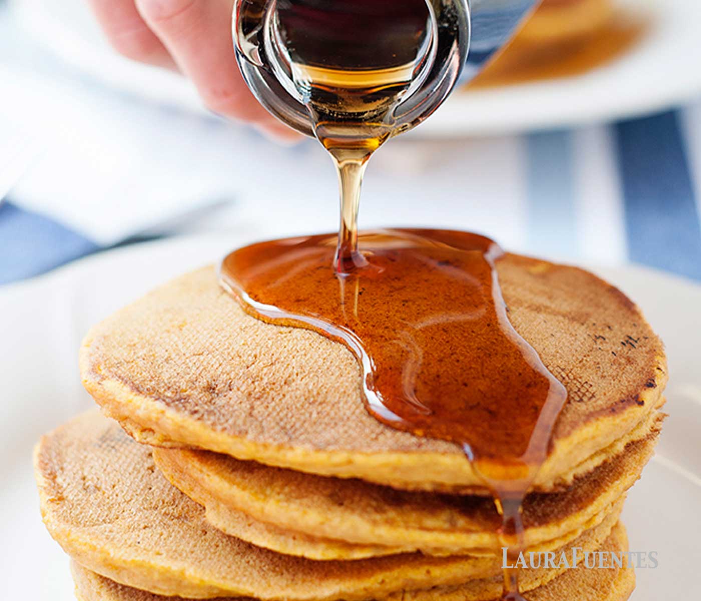 A stack of pumpkin pancakes being topped with maple syrup on a white plate. 