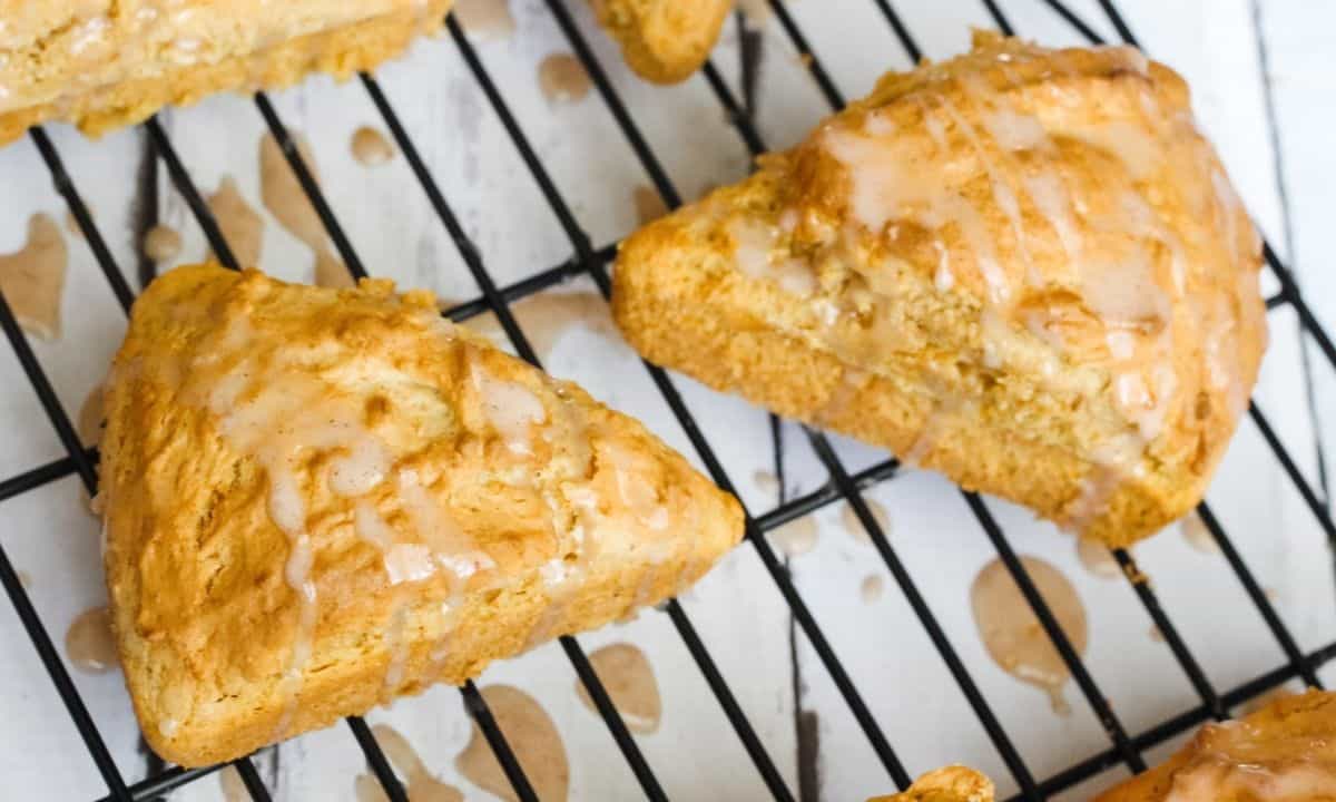 two pumpkin scones with glaze on a cooling rack