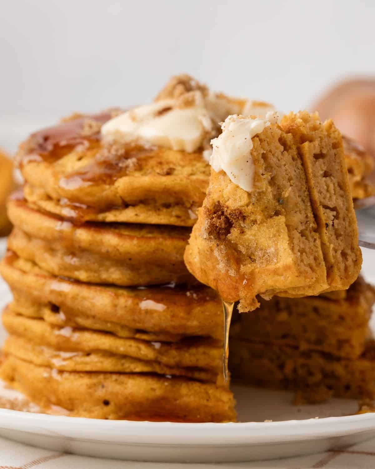 tall and fluffy stack of pumpkin pancakes on a plate topped with butter, brown sugar, cinnamon, and pancake syrup