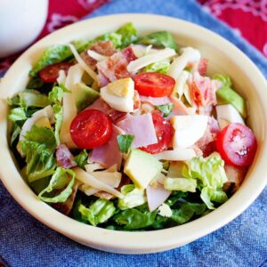 a bowl of cobb salad with ham, cheese, greens, hard boiled egg, and tomato