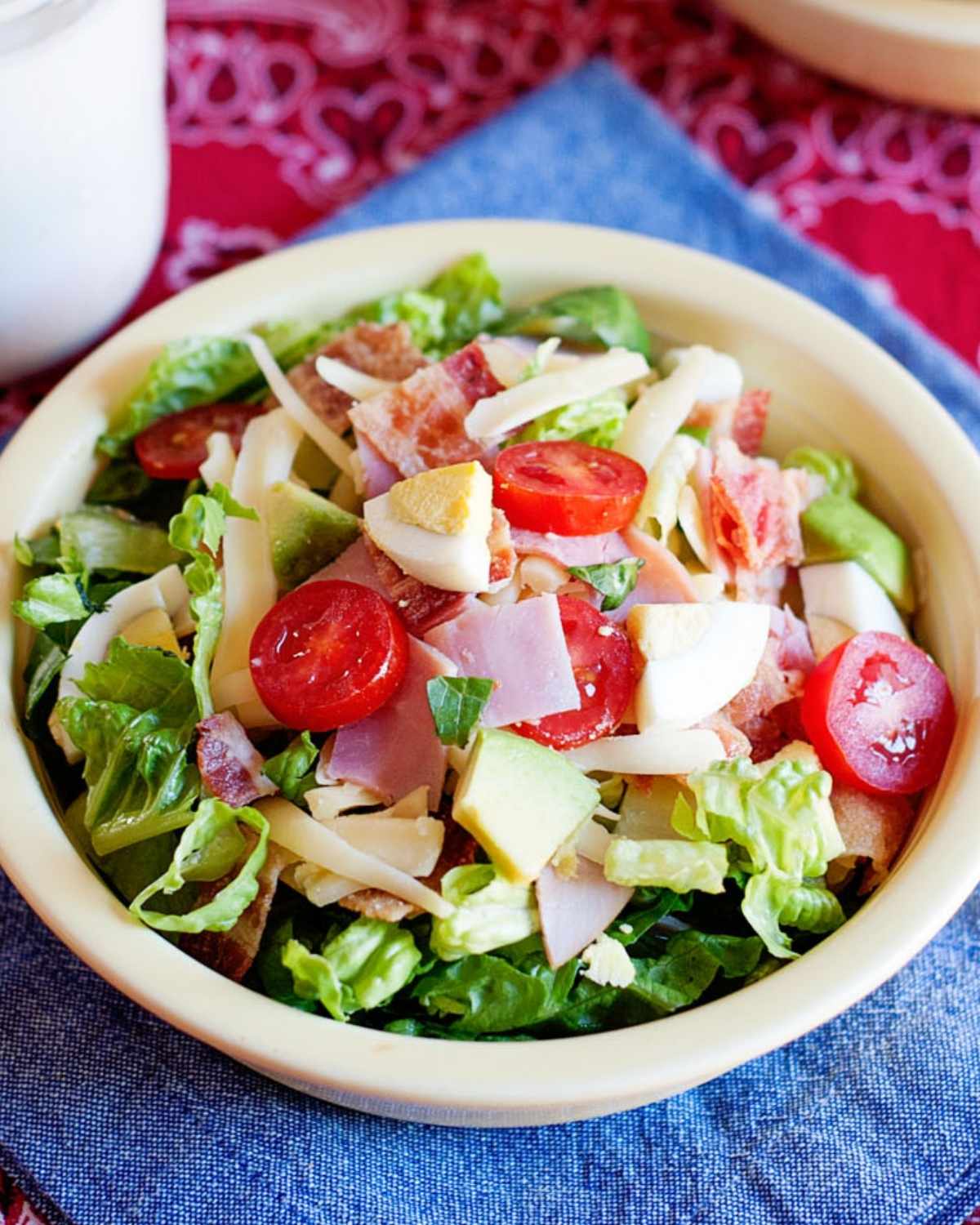 a bowl of cobb salad with ham, cheese, greens, hard boiled egg, and tomato