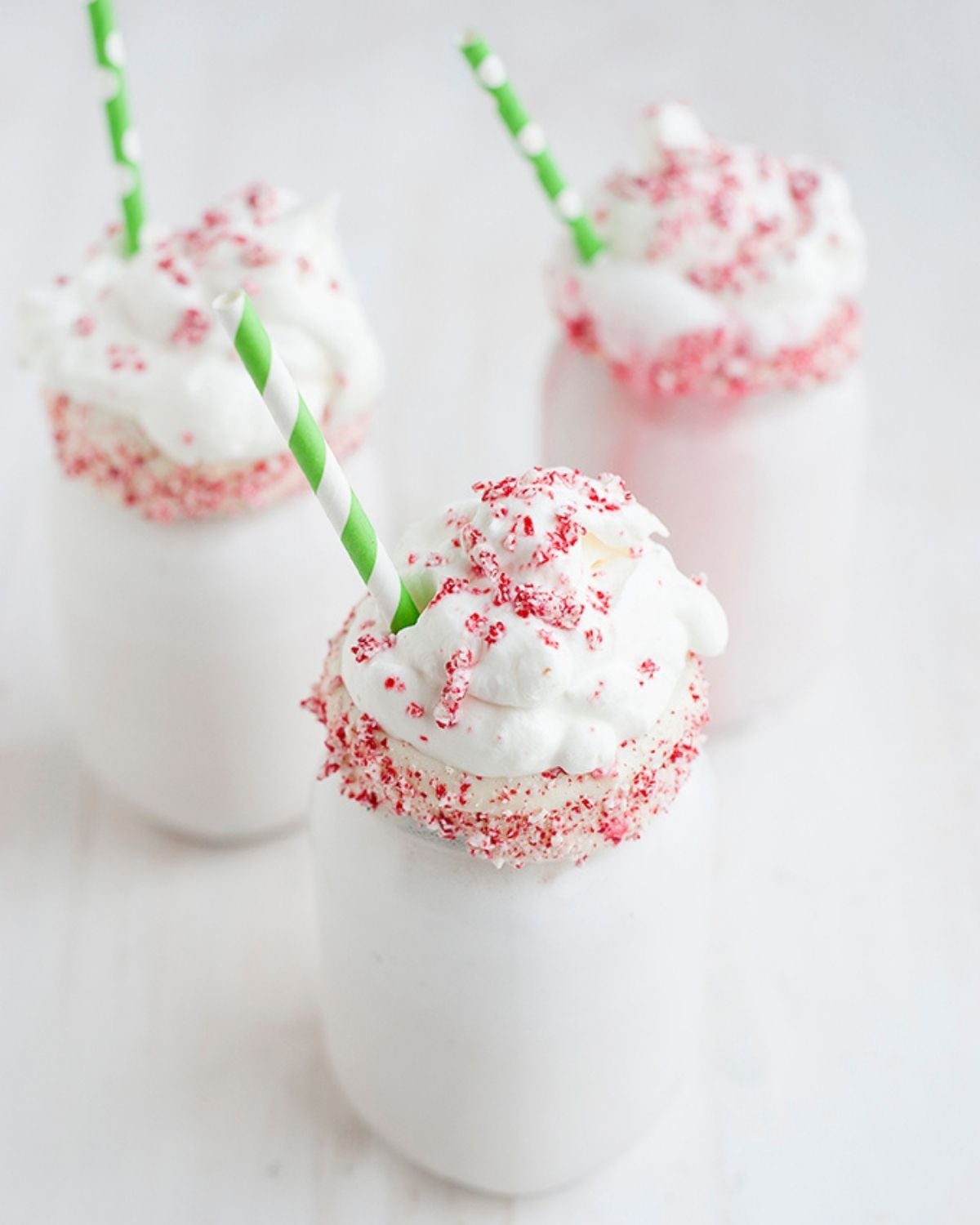 three peppermint milkshakes in a candy cane rimmed mason jar glass