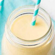 glass cup of mango peach smoothie with a blue and white striped straw
