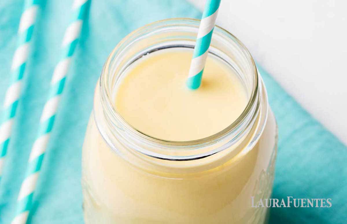 glass cup of mango peach smoothie with a blue and white striped straw
