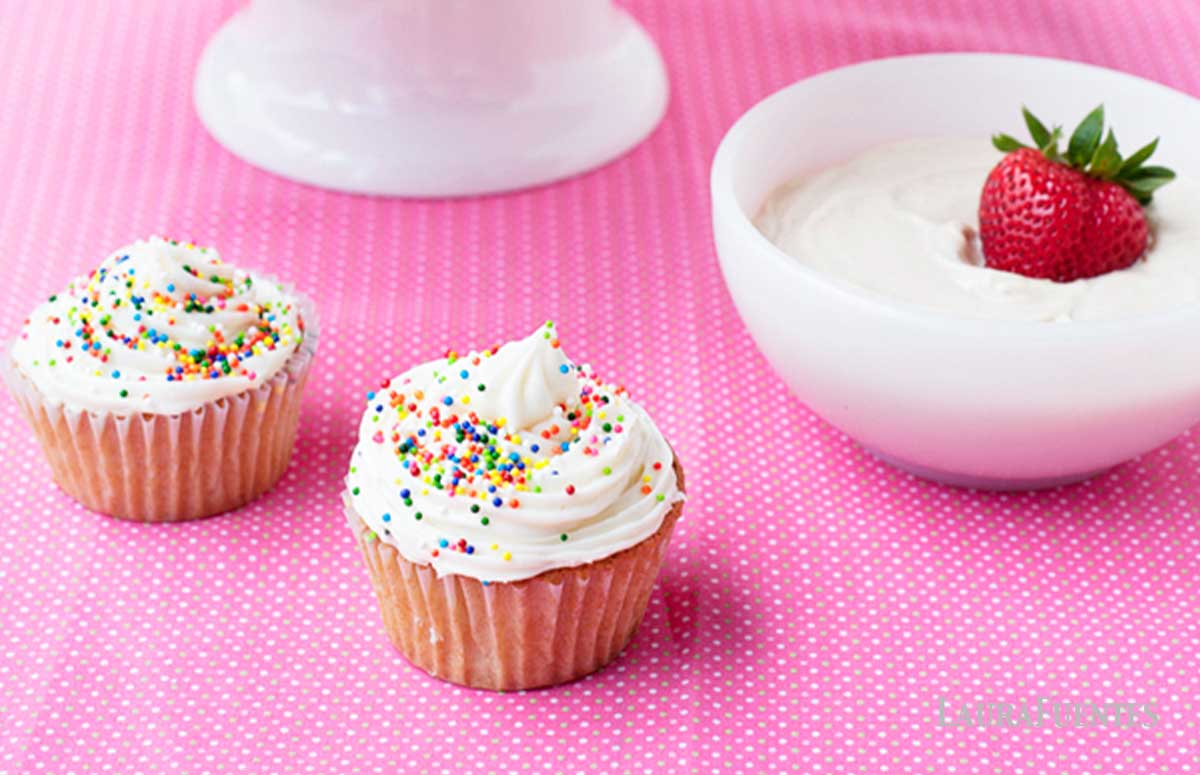 two birthday cupcakes made with greek yogurt next to a bowl with frosting