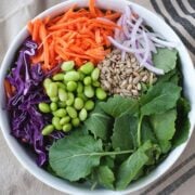 top view of a white bowl with edamame, kale, red cabbage, shredded carrot, onion and seeds