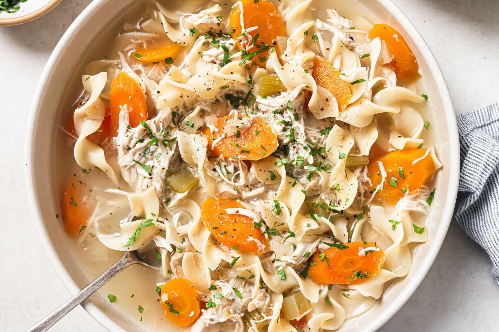 overhead view of a bowl of chicken noodle soup made with rotisserie chicken, egg noodles, carrots, celery, and a rich broth