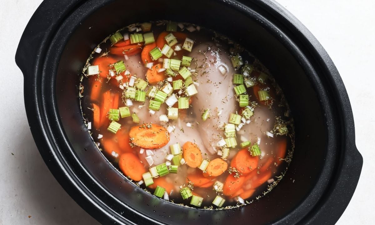 top view of slow cooker with raw chicken, veggies, and liquid