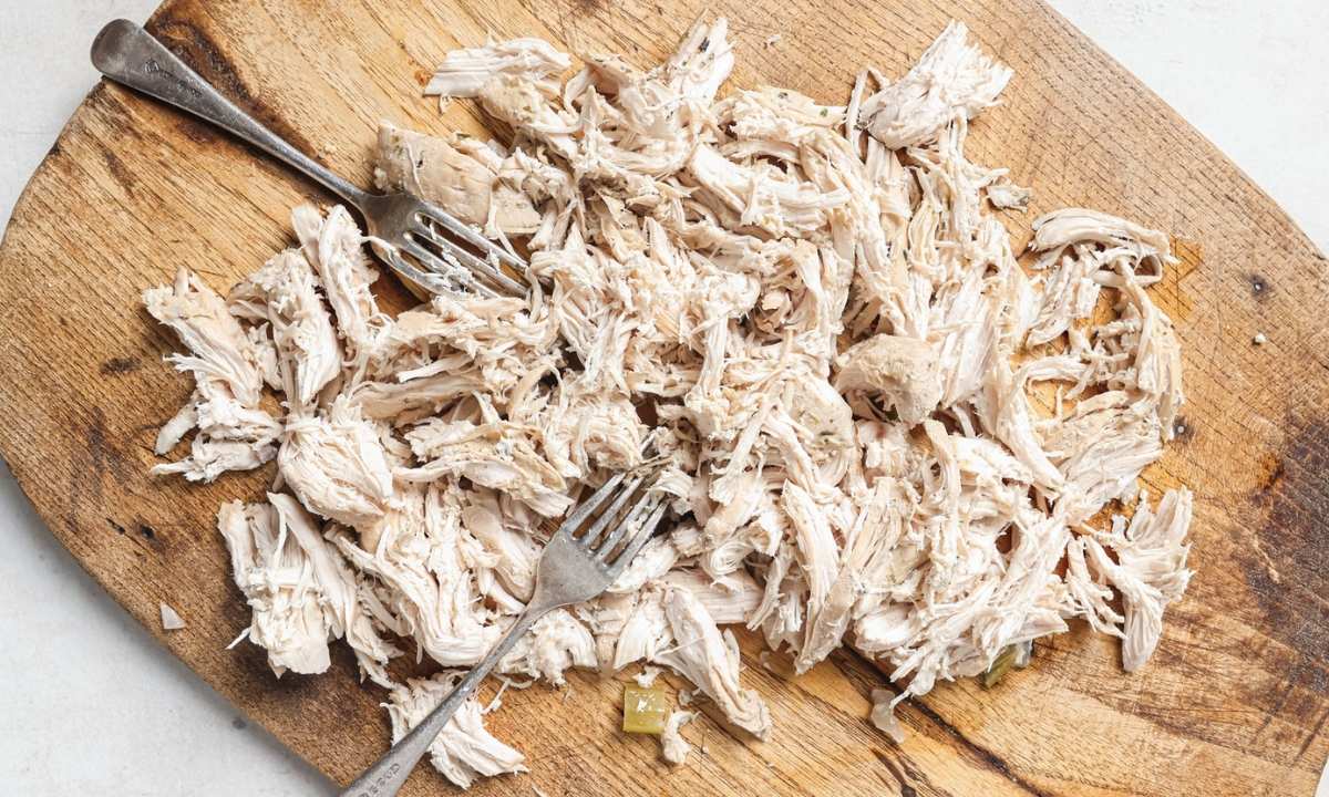 top view of wooden board with two forks and shredded chicken