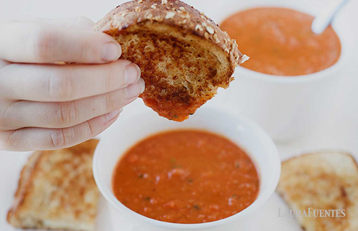 child dipping a slice of grilled cheese into small cup of tomato soup