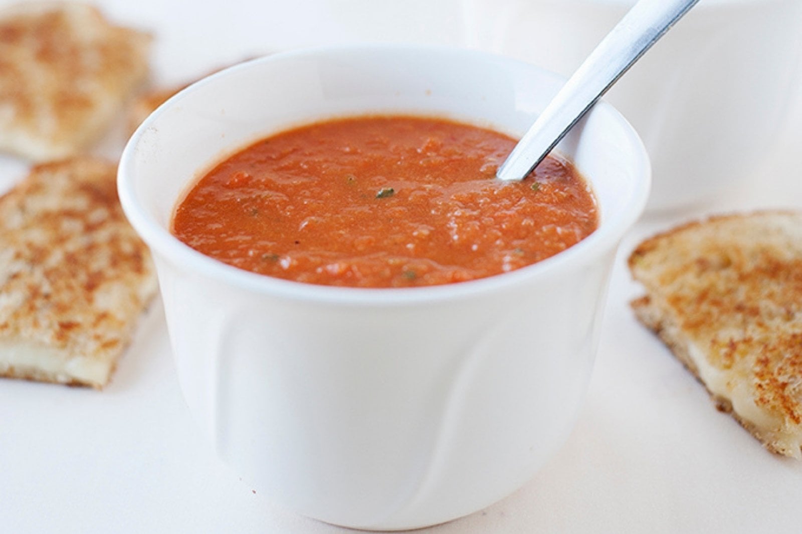 a small bowl of tomato soup with grilled cheese on the back