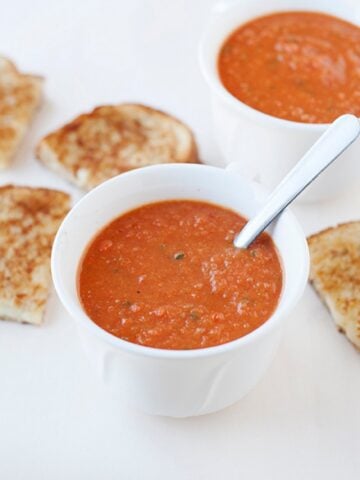 two small bowls of tomato soup with grilled cheese on the back