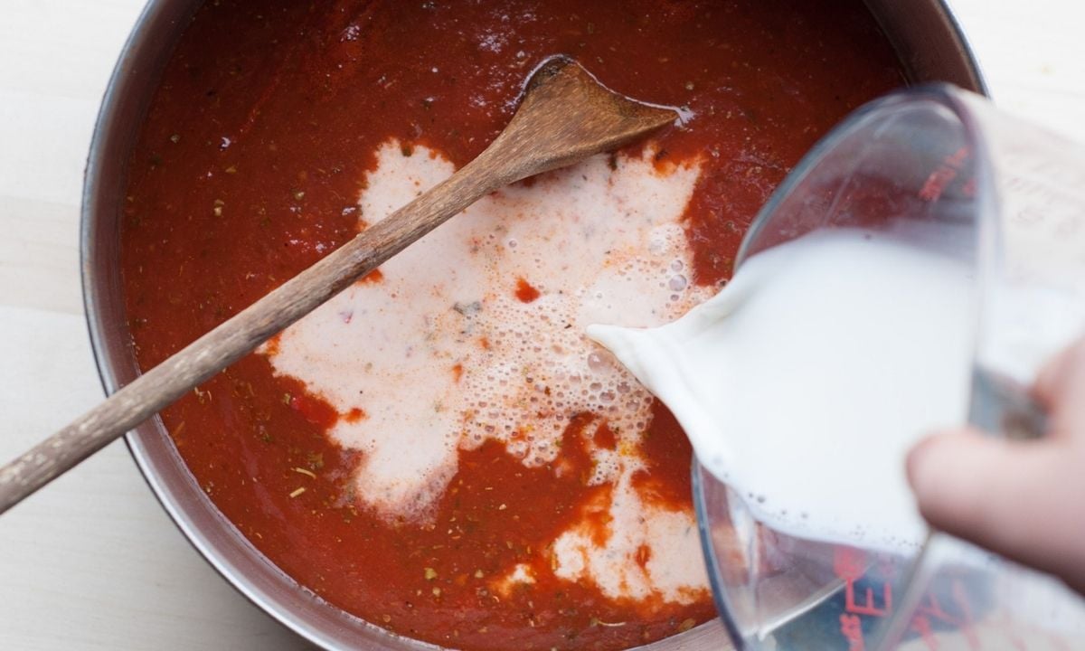 pouring half and half into a pot of tomato tortellini soup