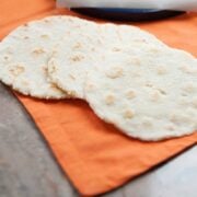 image: three grainless tortillas sitting on a counter next to a tortilla press nad balls of homemade tortilla dough