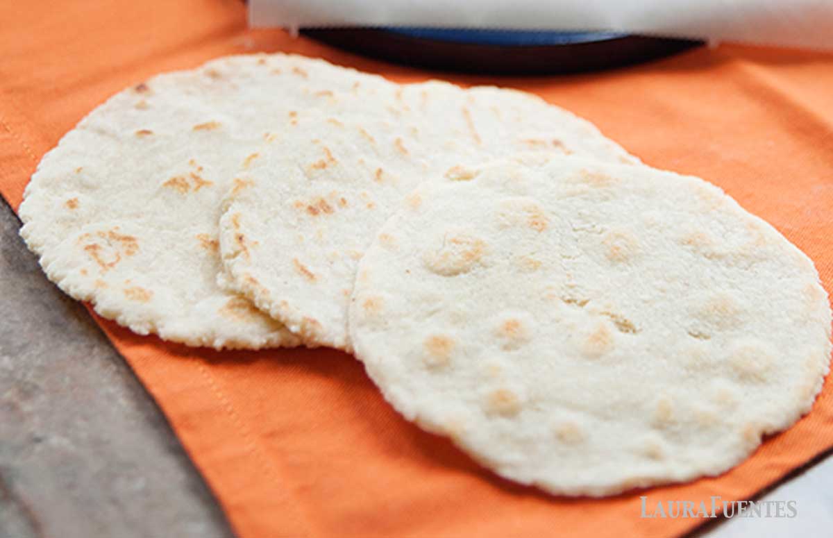 image: three grainless tortillas sitting on a counter next to a tortilla press nad balls of homemade tortilla dough