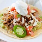 pork carnitas served in a tostada and topped with jalapeño slices, pico de gallo and sour cream