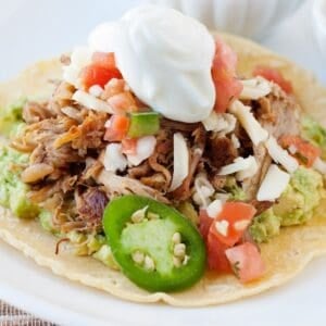 pork carnitas served in a tostada and topped with jalapeño slices, pico de gallo and sour cream