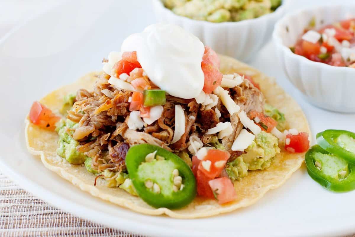 pork carnitas served in a tostada and topped with jalapeño slices, pico de gallo and sour cream